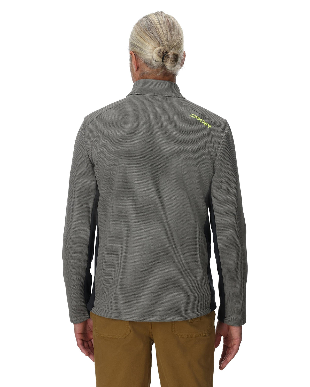 Person wearing a gray jacket with a brand logo on the back, standing against a white background