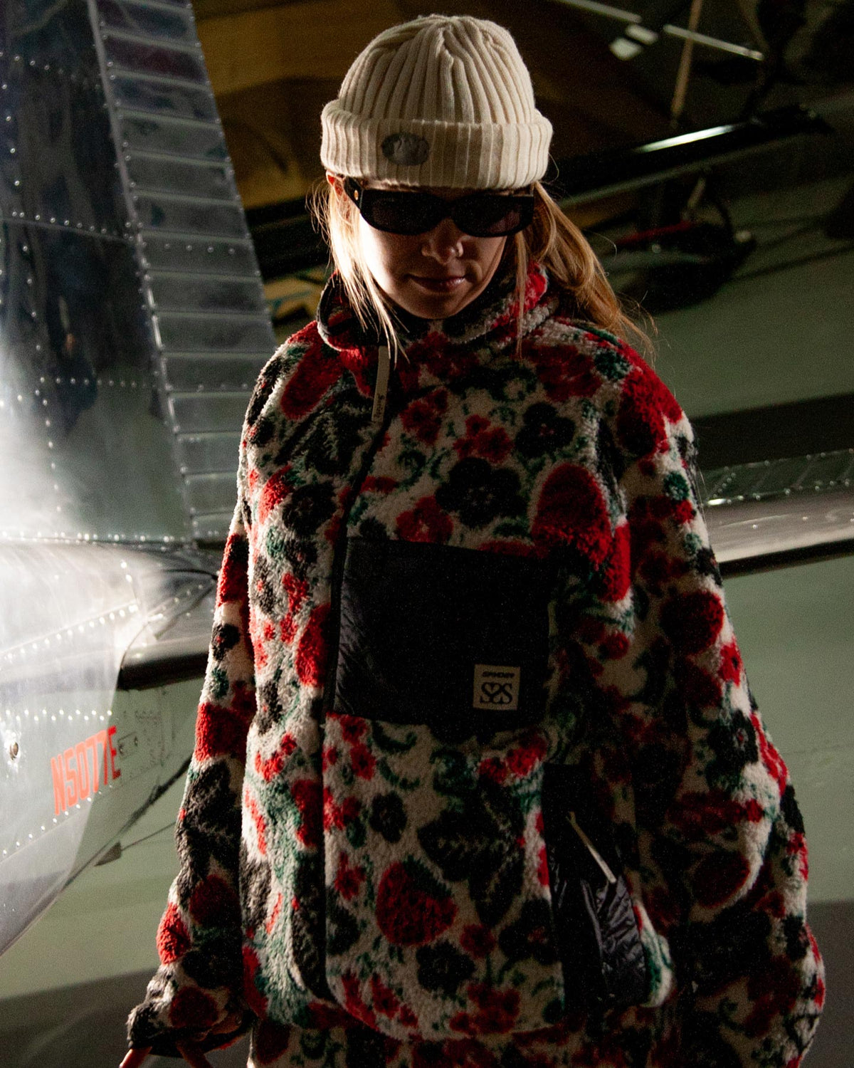 Person wearing a colorful coat and white beanie in front of an airplane
