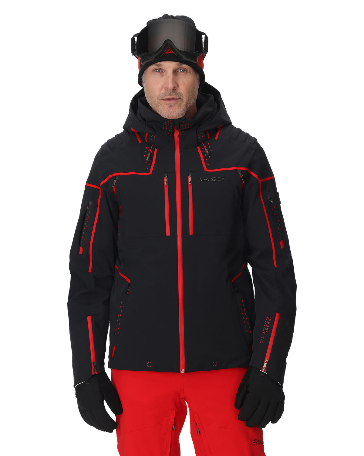 Person wearing a black and red ski jacket with goggles on a white background