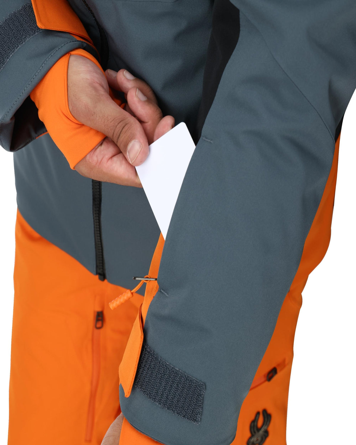 Close-up of a person wearing an orange and gray jacket with a white card in the pocket.
