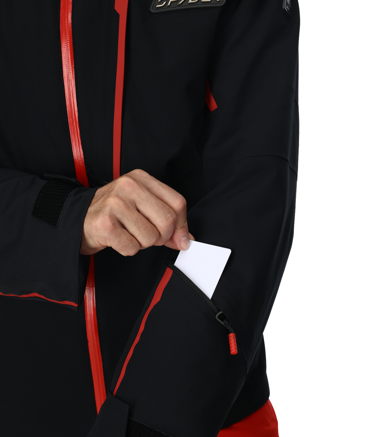 Person wearing a black jacket with red zippers, pulling out a white card from a pocket.