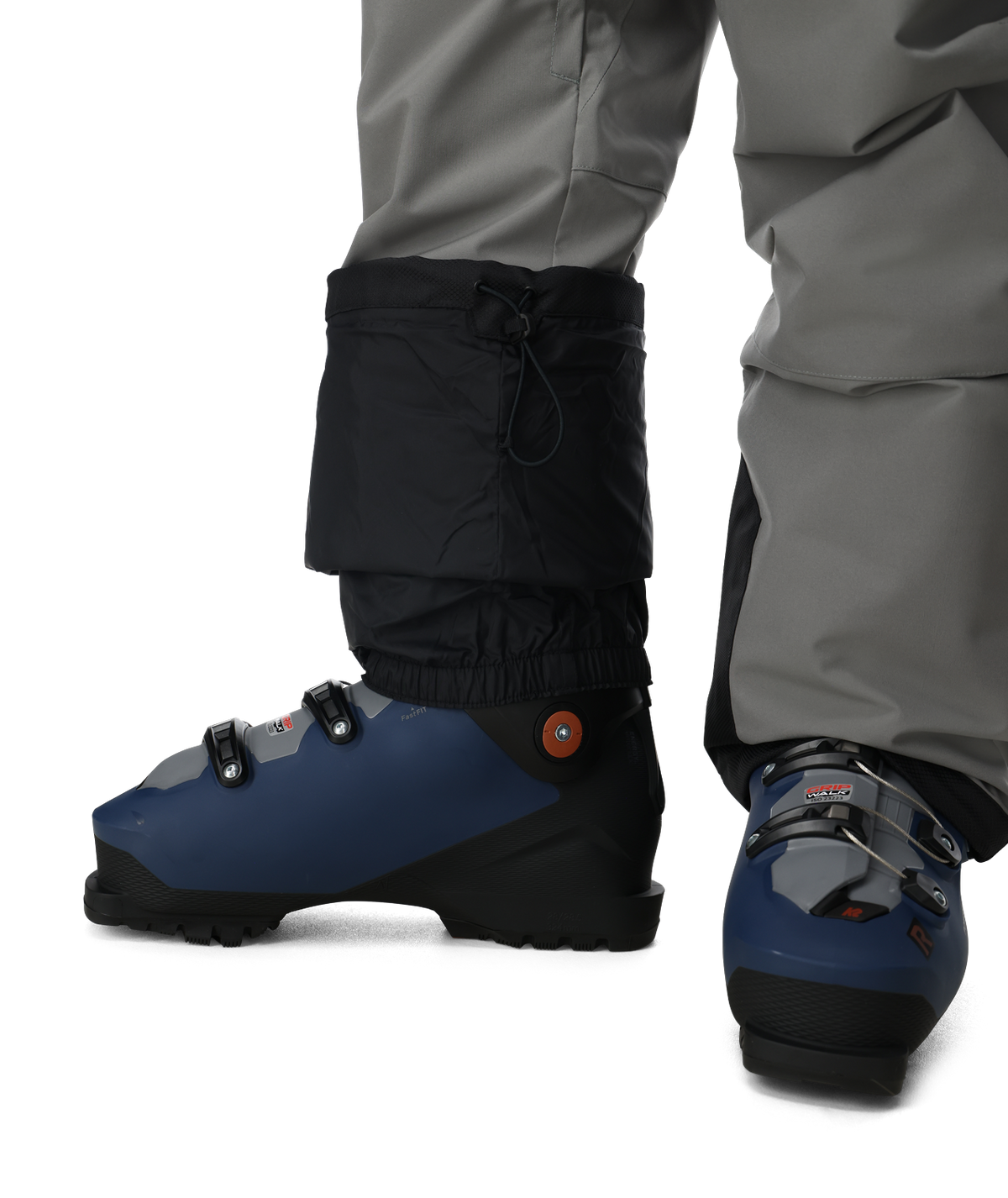Blue ski boots with black gaiters worn by a person in gray pants on a white background