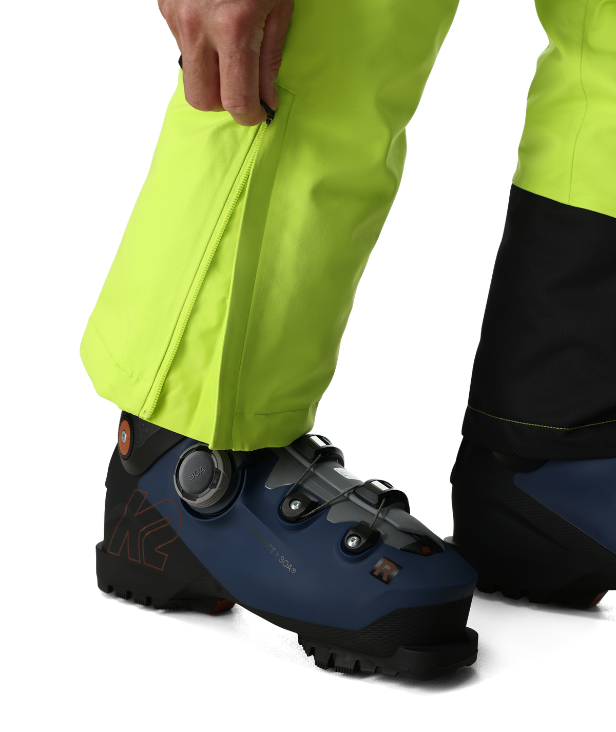Close-up of a person wearing bright yellow pants and blue ski boots on a white background