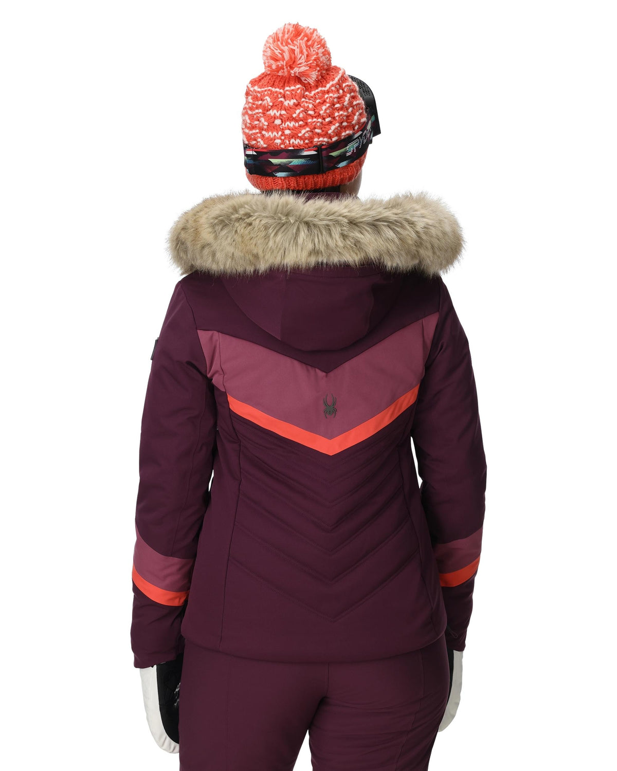 Person wearing a maroon winter jacket with fur hood and red accents, standing against a white background.