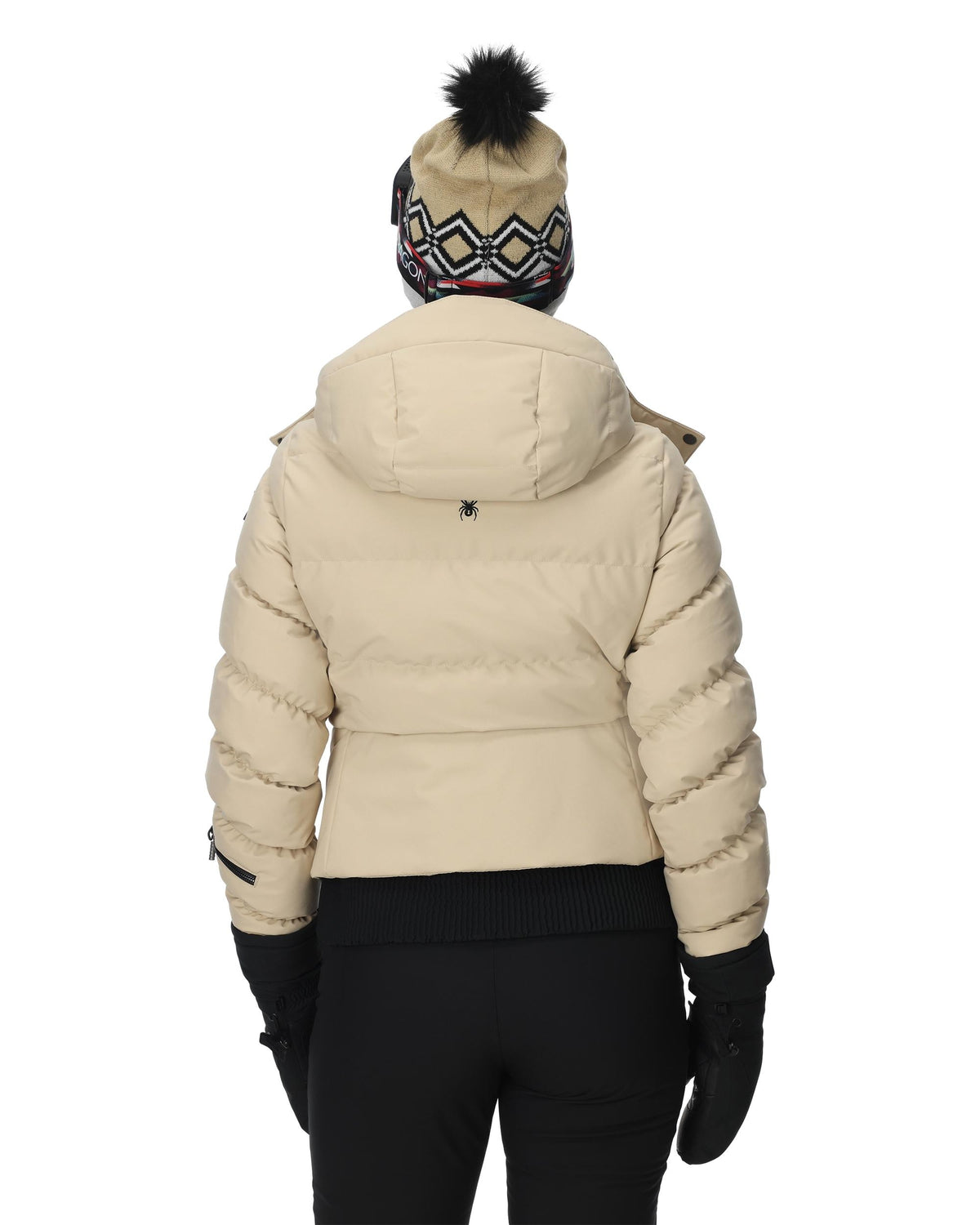 Person wearing a beige puffer jacket, black pants, and a patterned beanie on a white background