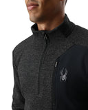 Person wearing a dark gray and black jacket with a logo on a white background