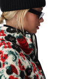 Person wearing a colorful floral-patterned jacket with a black beanie and sunglasses on a white background