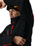 Man wearing a black jacket with red accents and goggles on his head against a white background