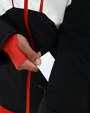 Person wearing a black and red jacket holding a white card.