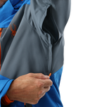 Close-up of a person wearing a gray and blue jacket with an orange zipper and logo.