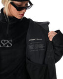 Person wearing a black jacket with logos on a white background
