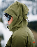 Person wearing a green hooded jacket with goggles on a blurred background