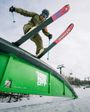 Person skiing on a green rail with 'Atomic' skis in a snowy landscape.