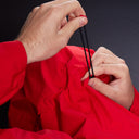 Person adjusting the drawstring of a red jacket against a dark background