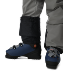 Blue ski boots with black gaiters worn by a person in gray pants on a white background