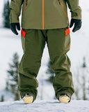 Person wearing green snow pants with orange accents in a snowy landscape