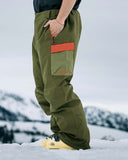 Person wearing green snow pants with orange pocket on a snowy background