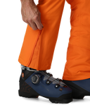 Person wearing orange ski pants with blue ski boots on a white background