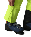 Close-up of a person wearing bright yellow pants and blue ski boots on a white background