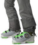 Gray ski boots with green accents worn with gray pants on a white background