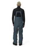 Person wearing a dark blue bib overalls with a black long-sleeve shirt on a white background