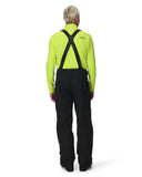 Person wearing a bright green jacket and black pants with suspenders on a white background