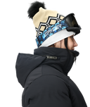 Person wearing a black jacket, patterned beanie with pom-pom, and goggles on a white background