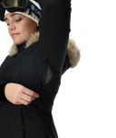 Person wearing a black coat with fur-lined hood and cuffs on a white background