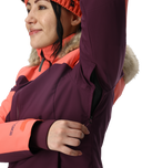 Person wearing a purple and pink winter jacket with fur-lined hood on a white background