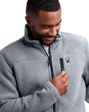Man wearing a gray fleece jacket with a brand logo, holding a pen.
