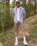 Man in plaid shirt and shorts standing in a forested area
