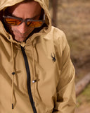 Person wearing a beige jacket with a hood and sunglasses, standing outdoors.