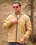 Man wearing a beige jacket with a brand logo in a forest setting