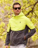 Man wearing a two-tone jacket with a logo in front of green foliage